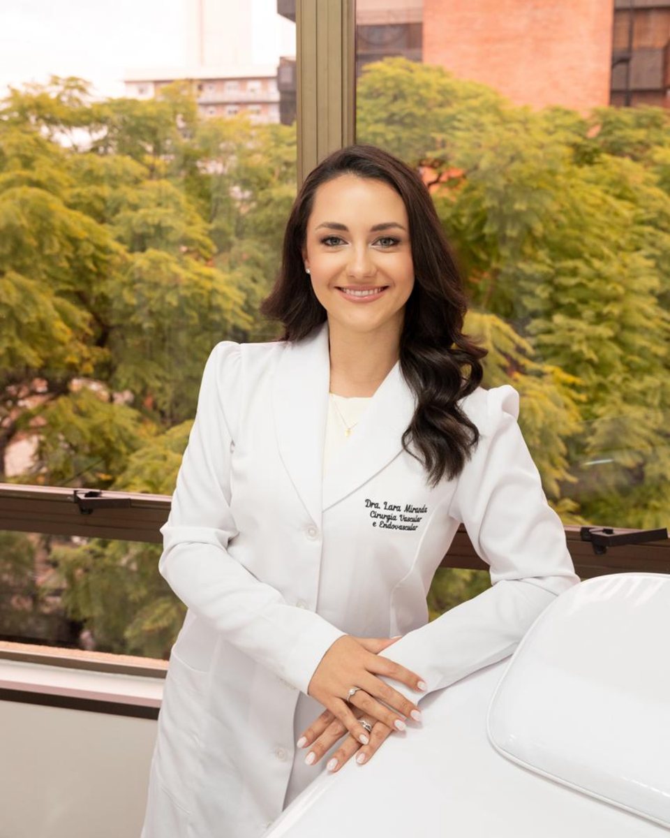 Dra. Lara Luz de Miranda Silva, de jaleco branco, em consultório com vista para árvores